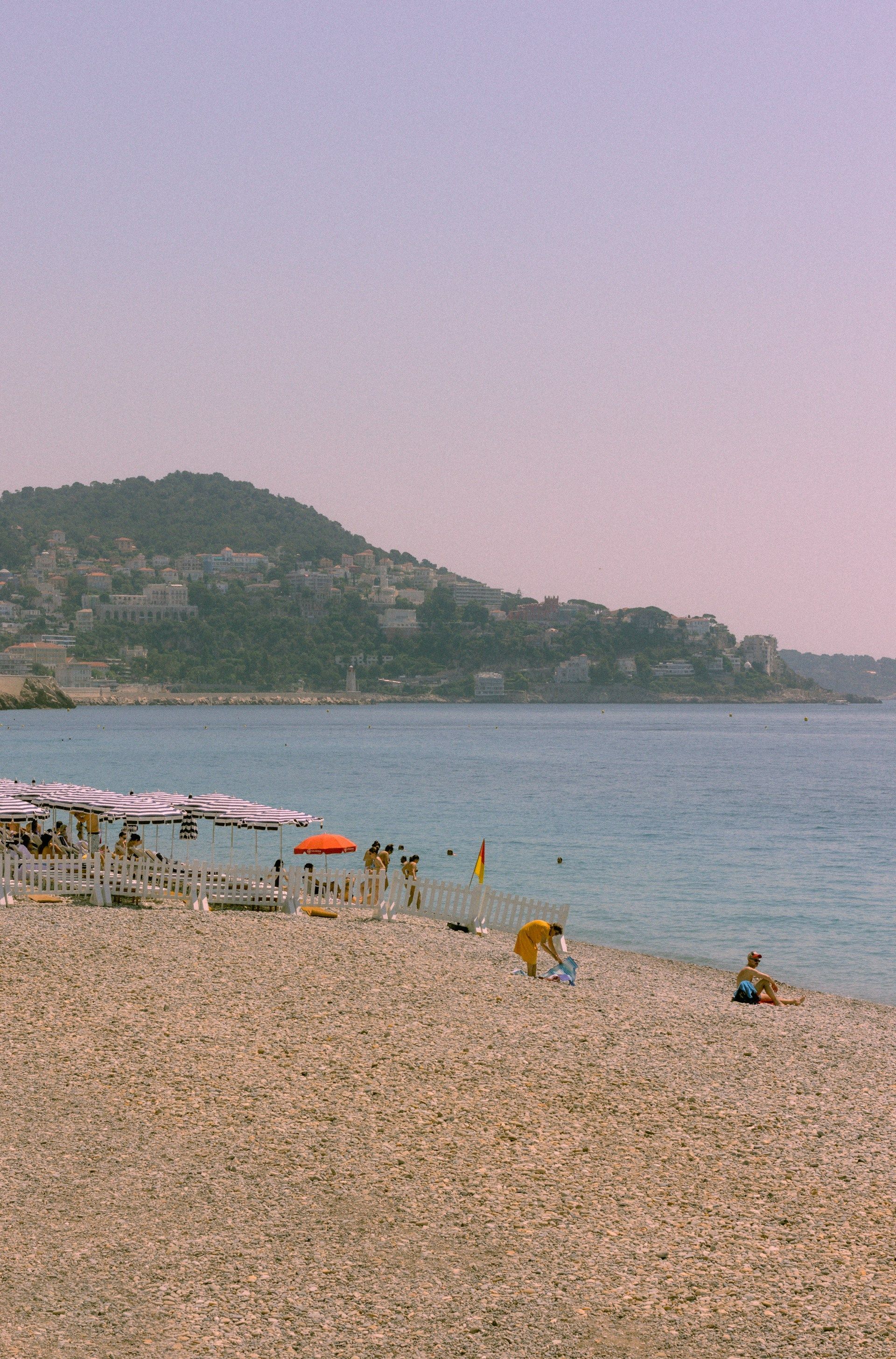 En strand med et fjell i bakgrunnen og folk som svømmer i vannet.