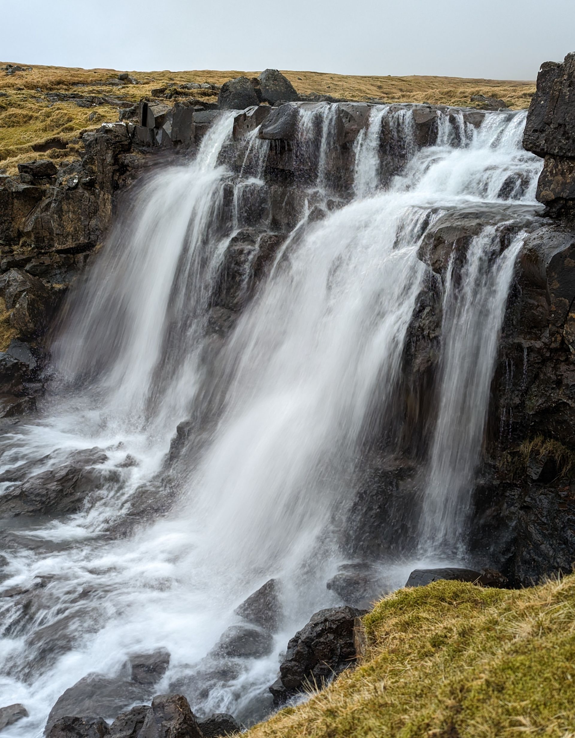 En foss er omgitt av steiner og gress i en åsside.