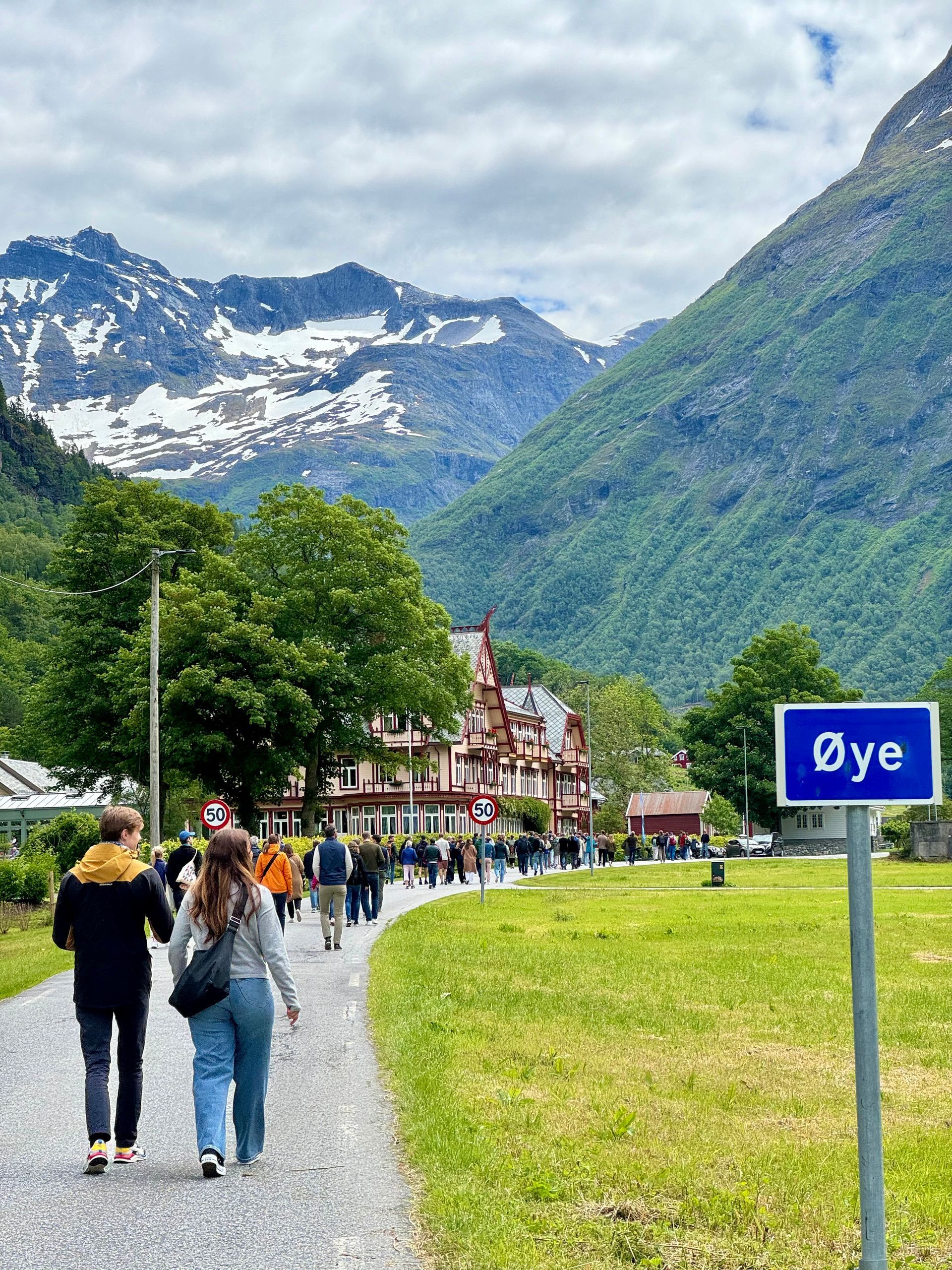 Et par mennesker som går nedover en sti med fjell i bakgrunnen.