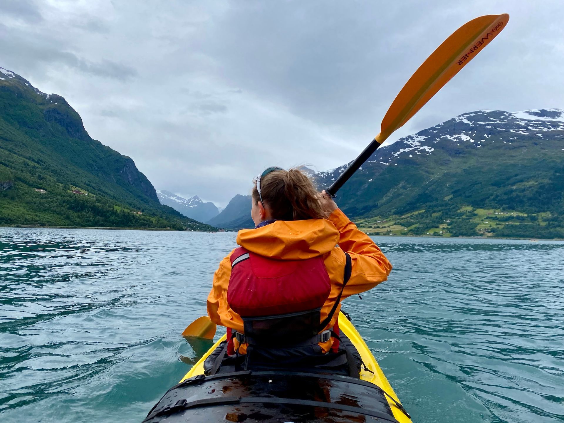 En person padler kajakk på en innsjø med fjell i bakgrunnen.