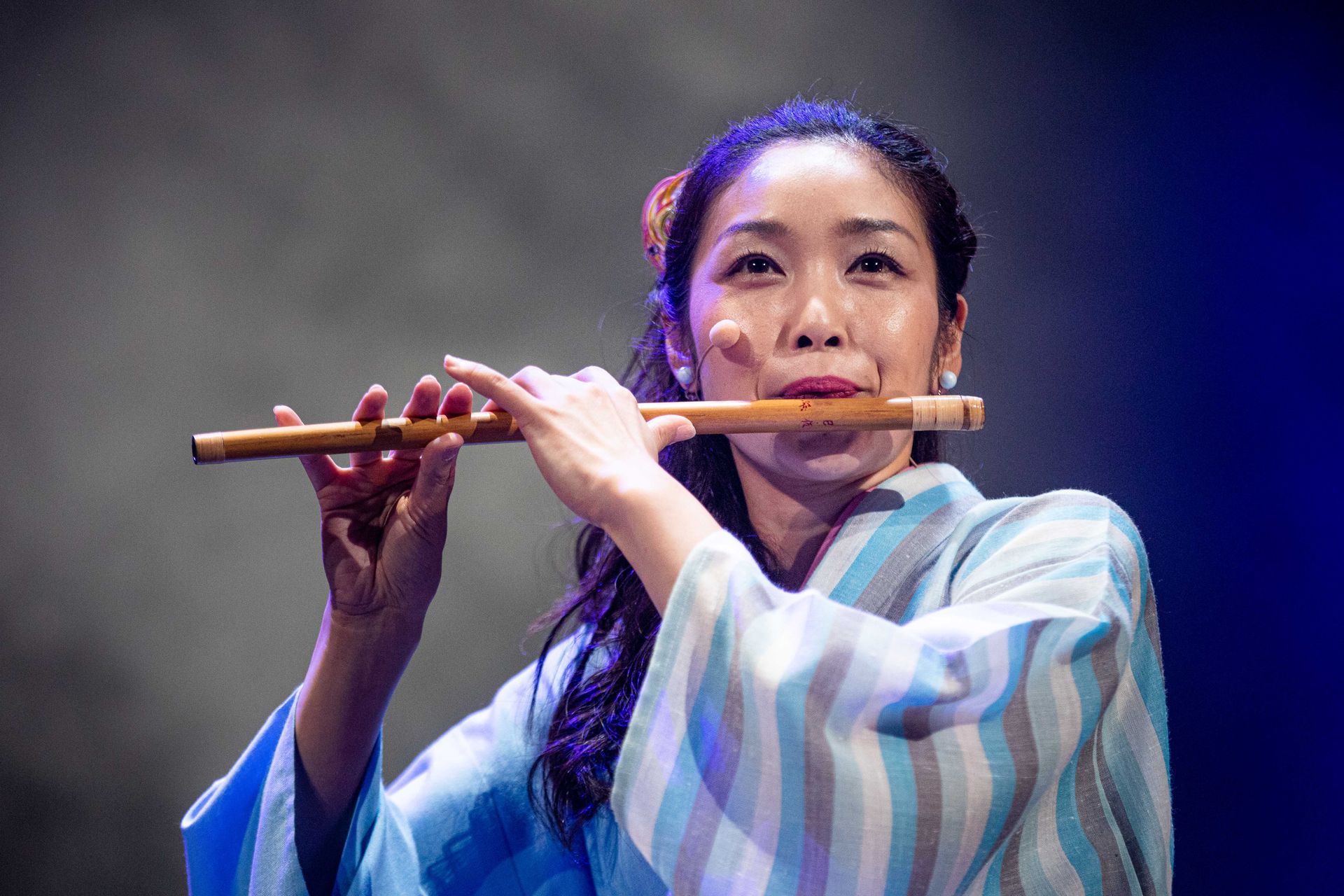 En kvinne i kimono spiller en fløyte på en scene.
