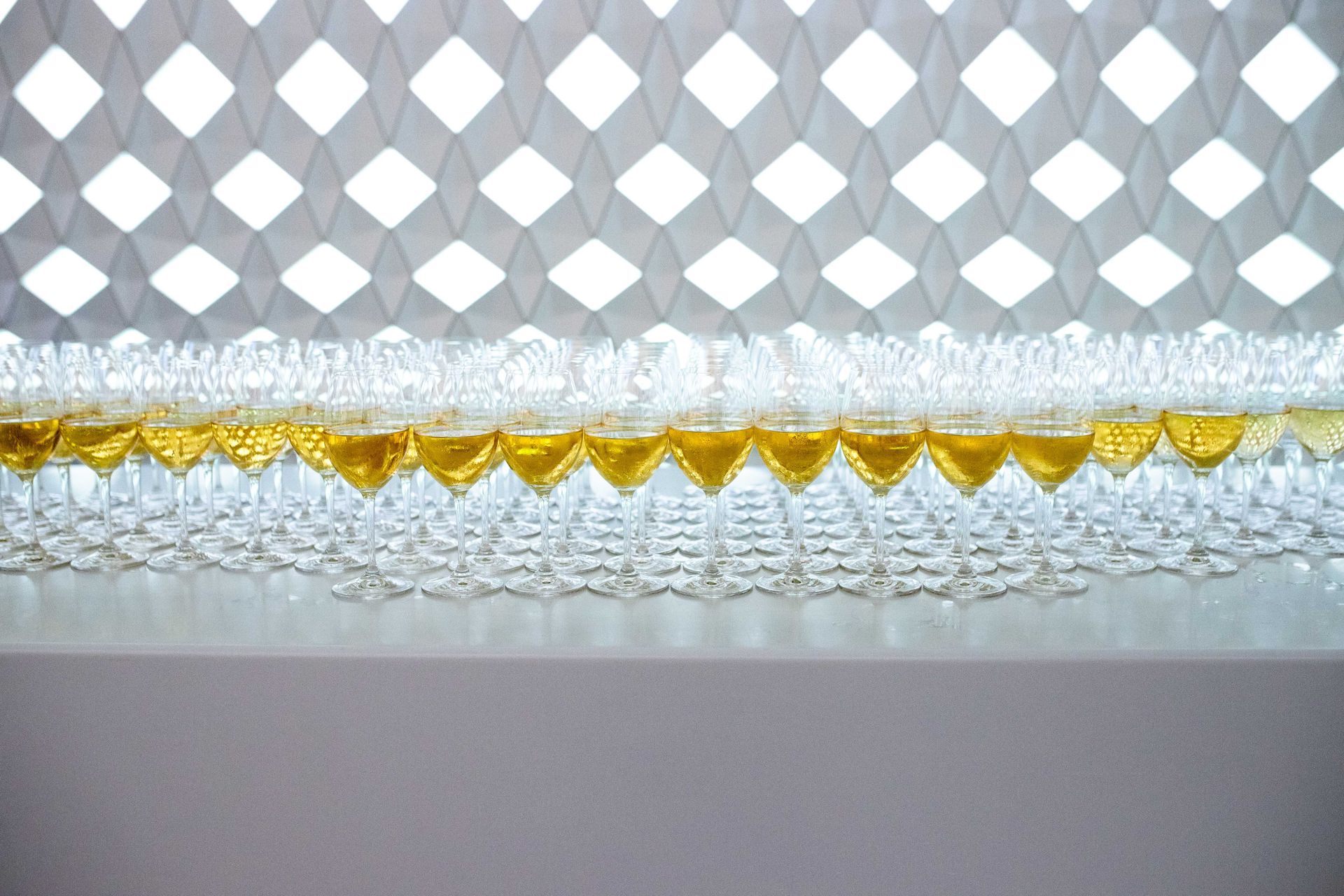 En rad med vinglass sitter på et bord foran et hvitt gittergjerde.