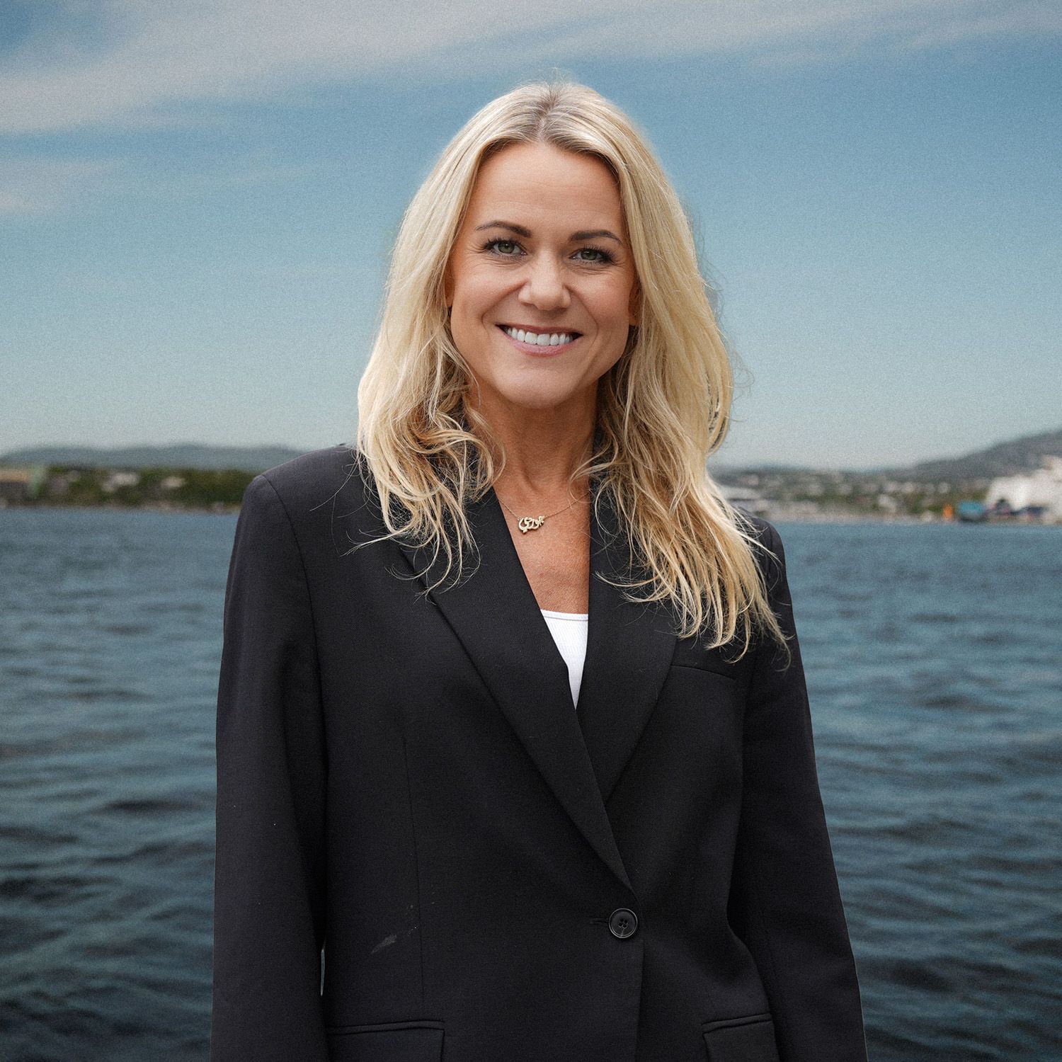 En mann med skjegg iført hvit skjorte står foran en vannmasse.