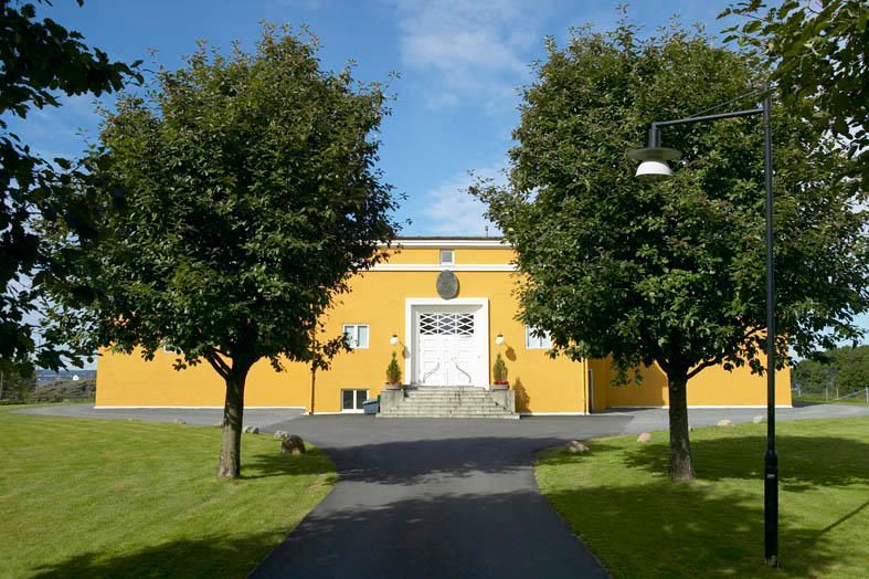 En gul bygning med en hvit dør er omgitt av trær