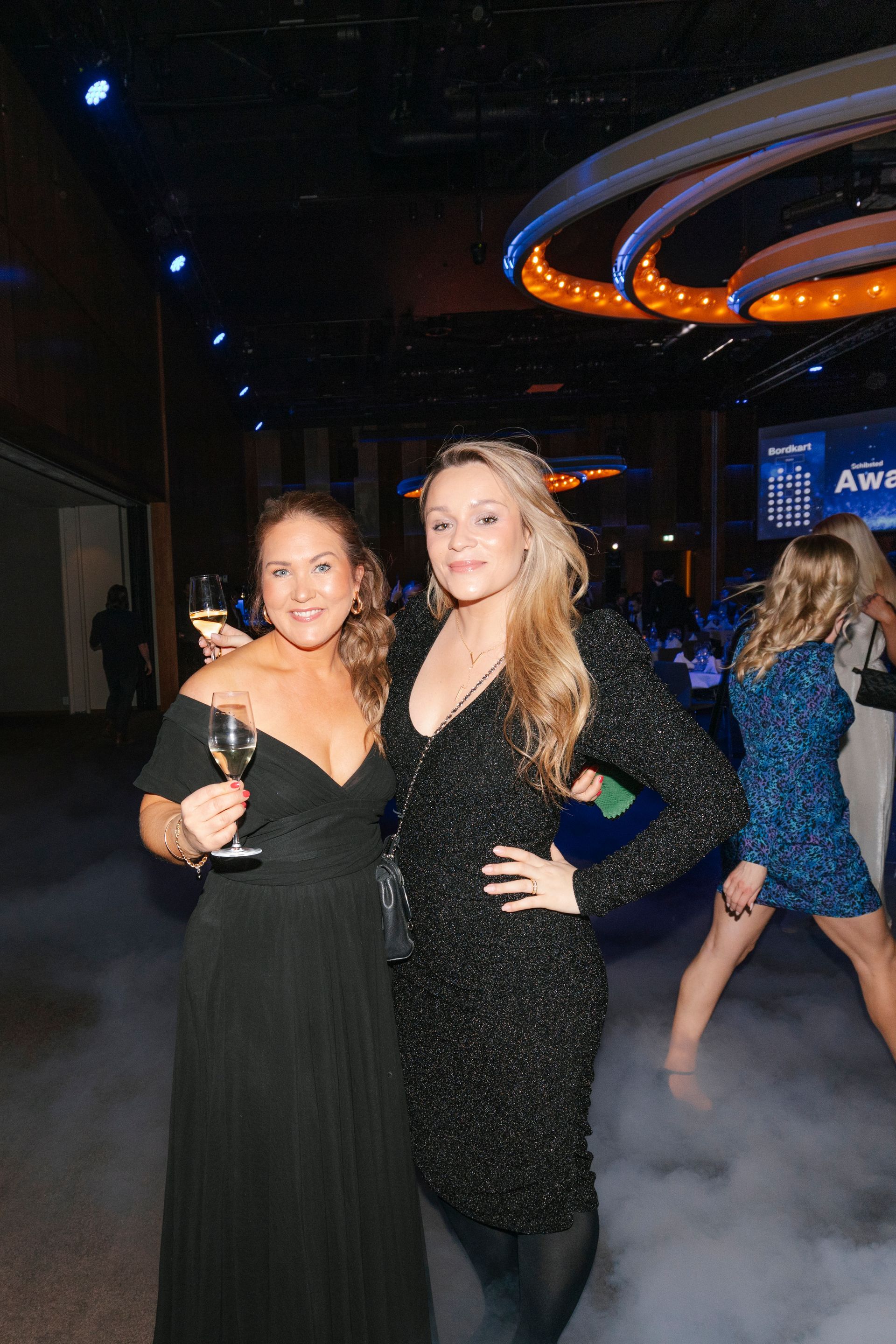 To kvinner poserer på en fest mens de holder vinglass.