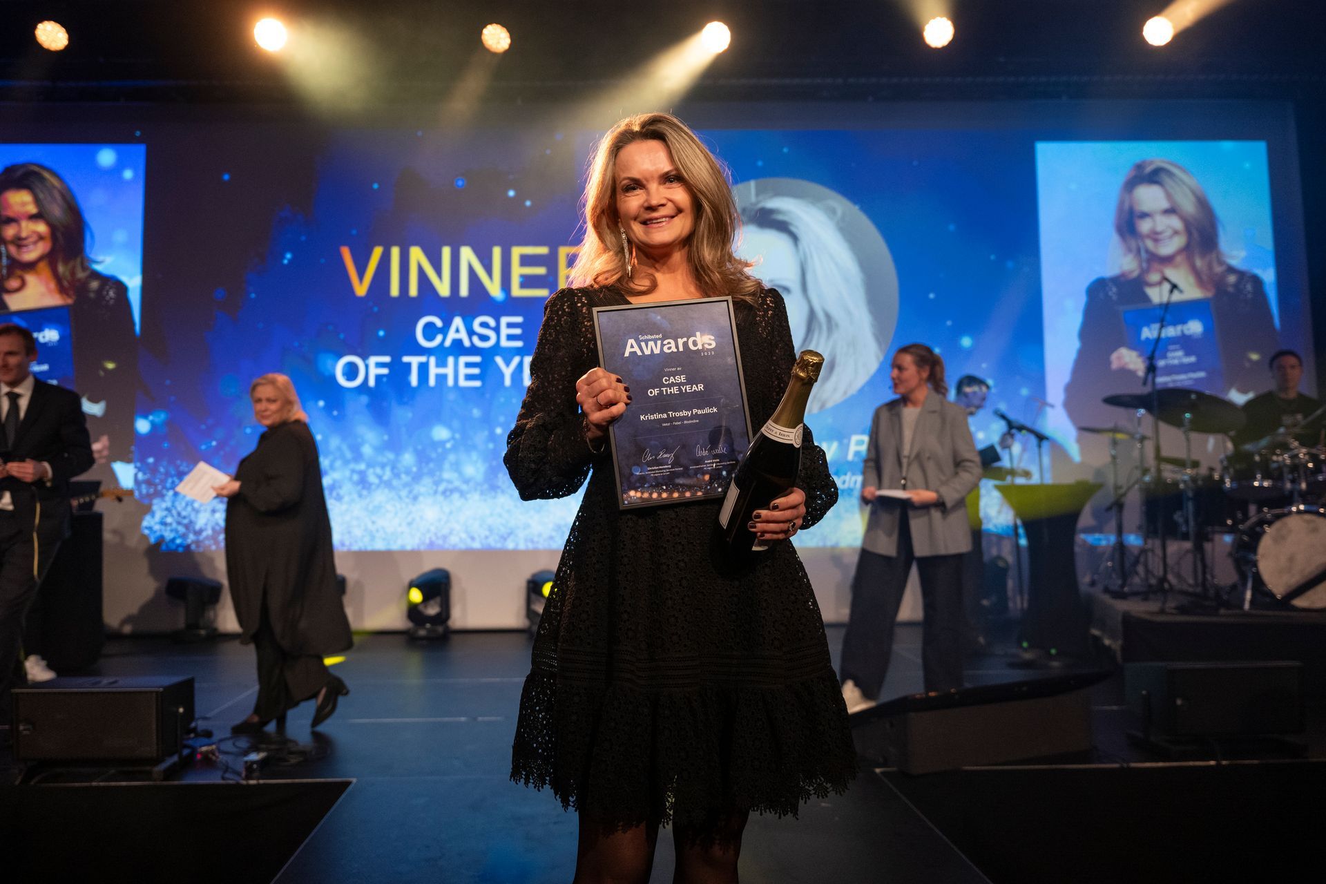 En kvinne står på en scene og holder et trofé og et sertifikat.