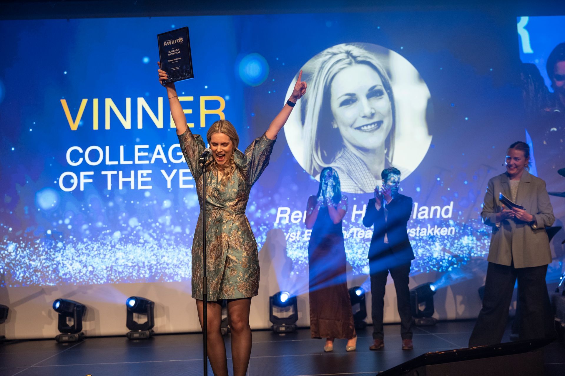 En kvinne står på en scene og holder et trofé.