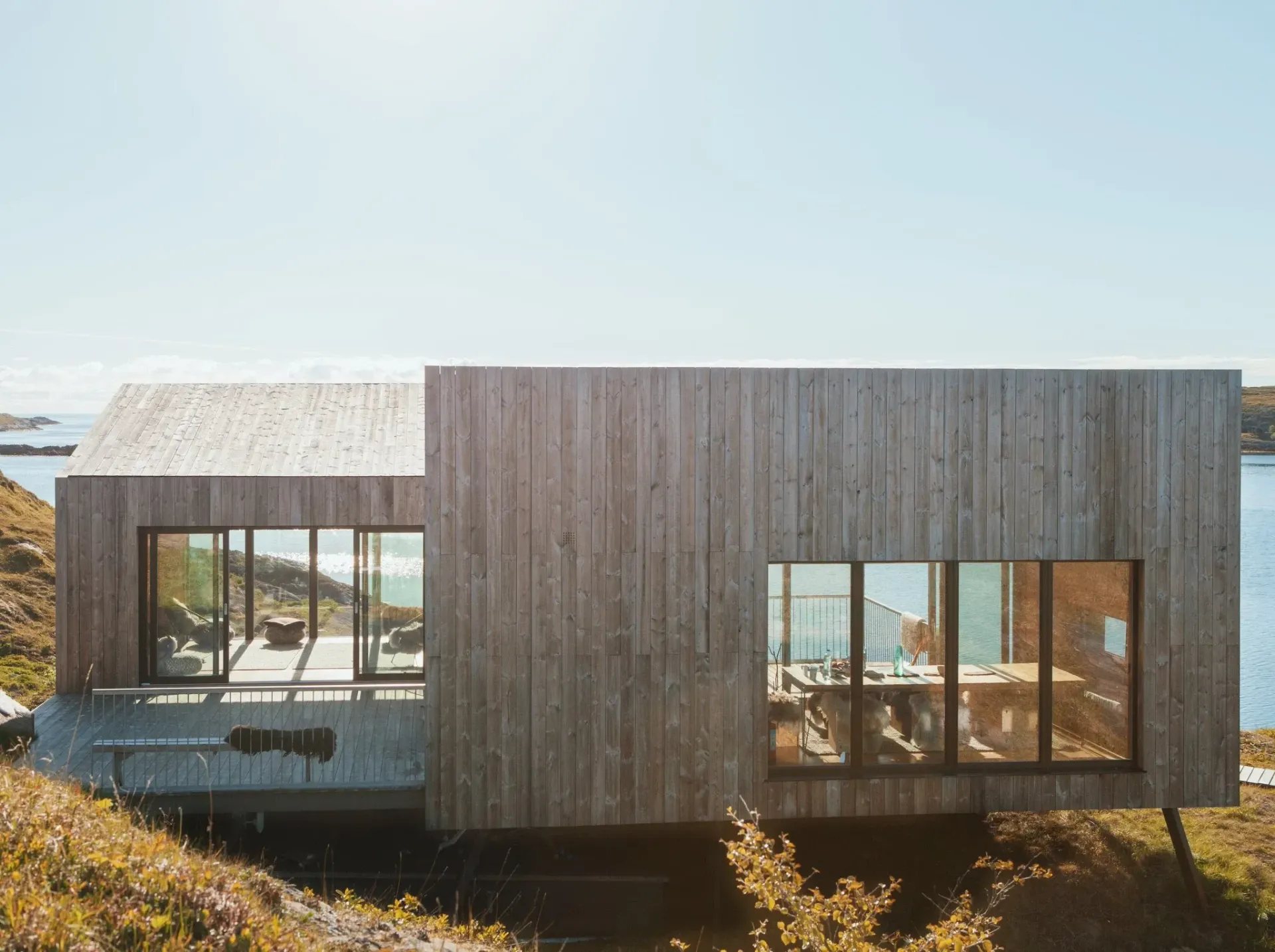 Et trehus sitter på toppen av en høyde ved siden av en vannmasse.