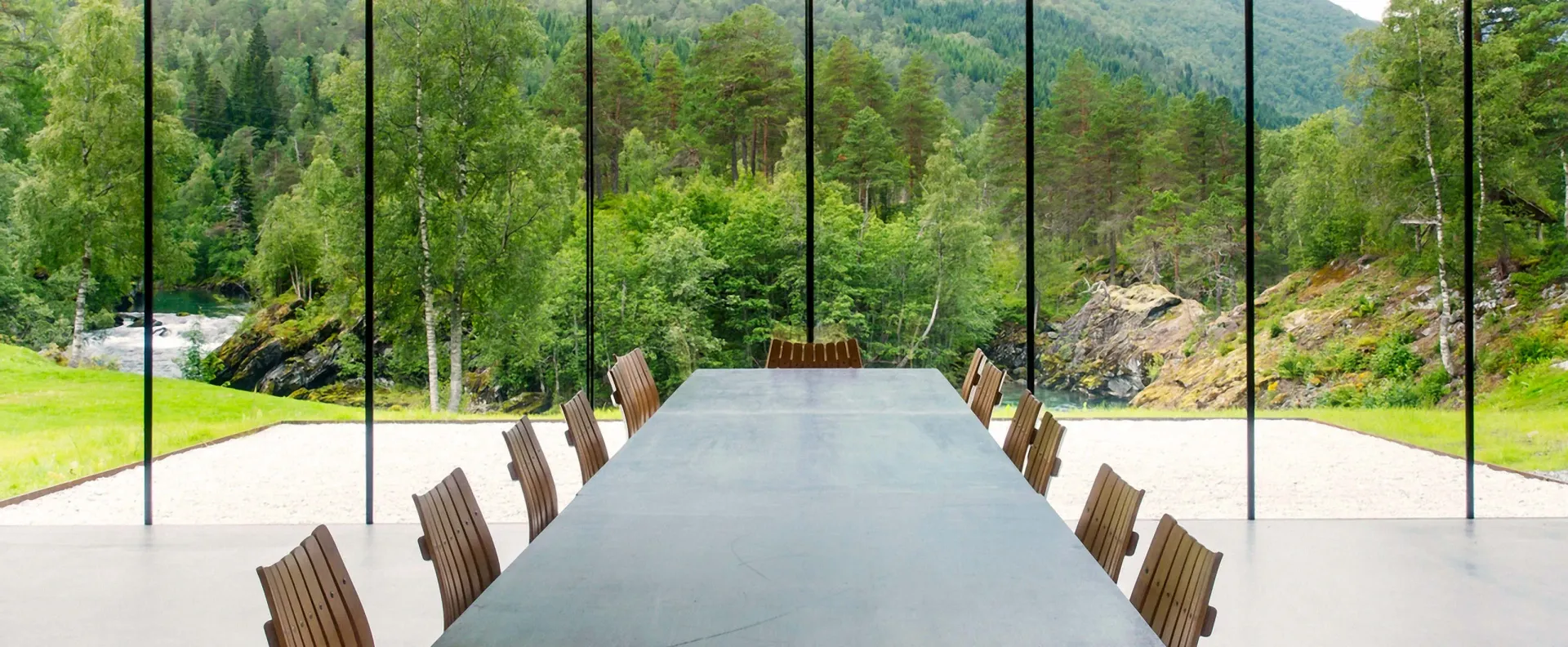 Et konferanserom med langbord og stoler og utsikt over en skog.