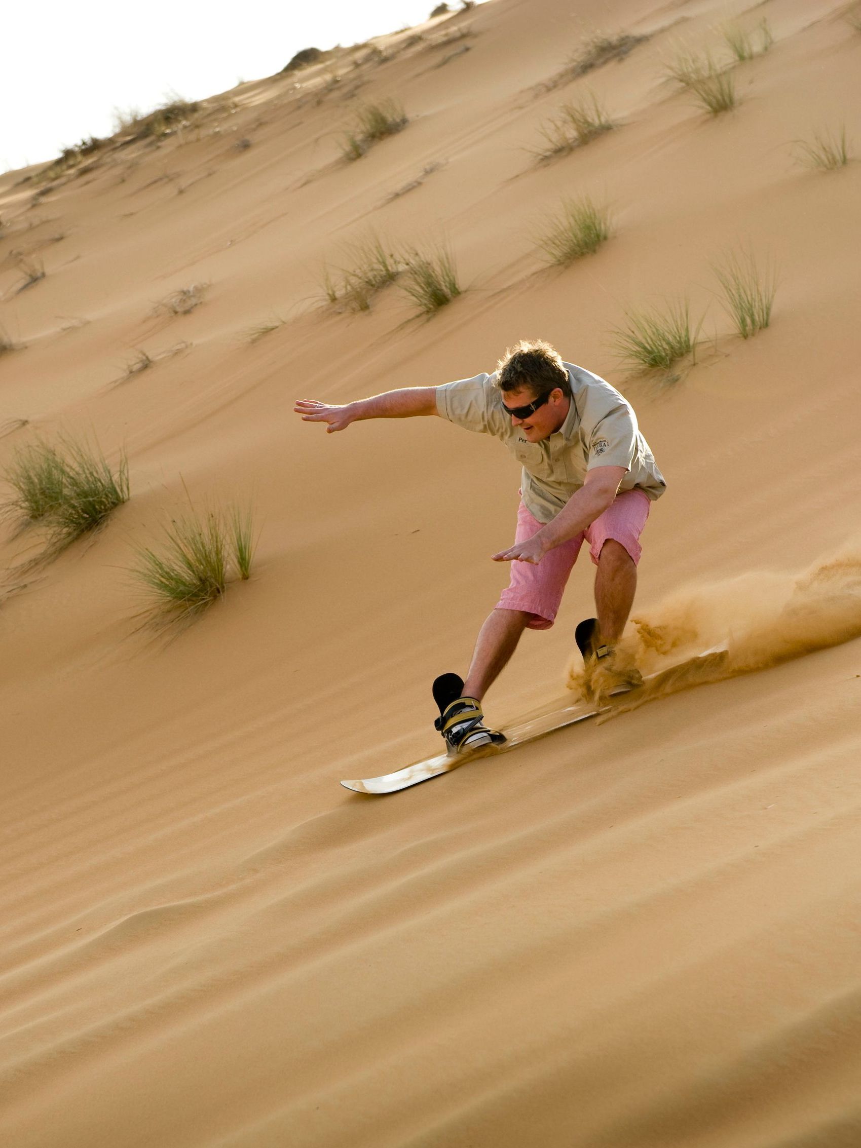 En mann går på sandbrett ned en sanddyne
