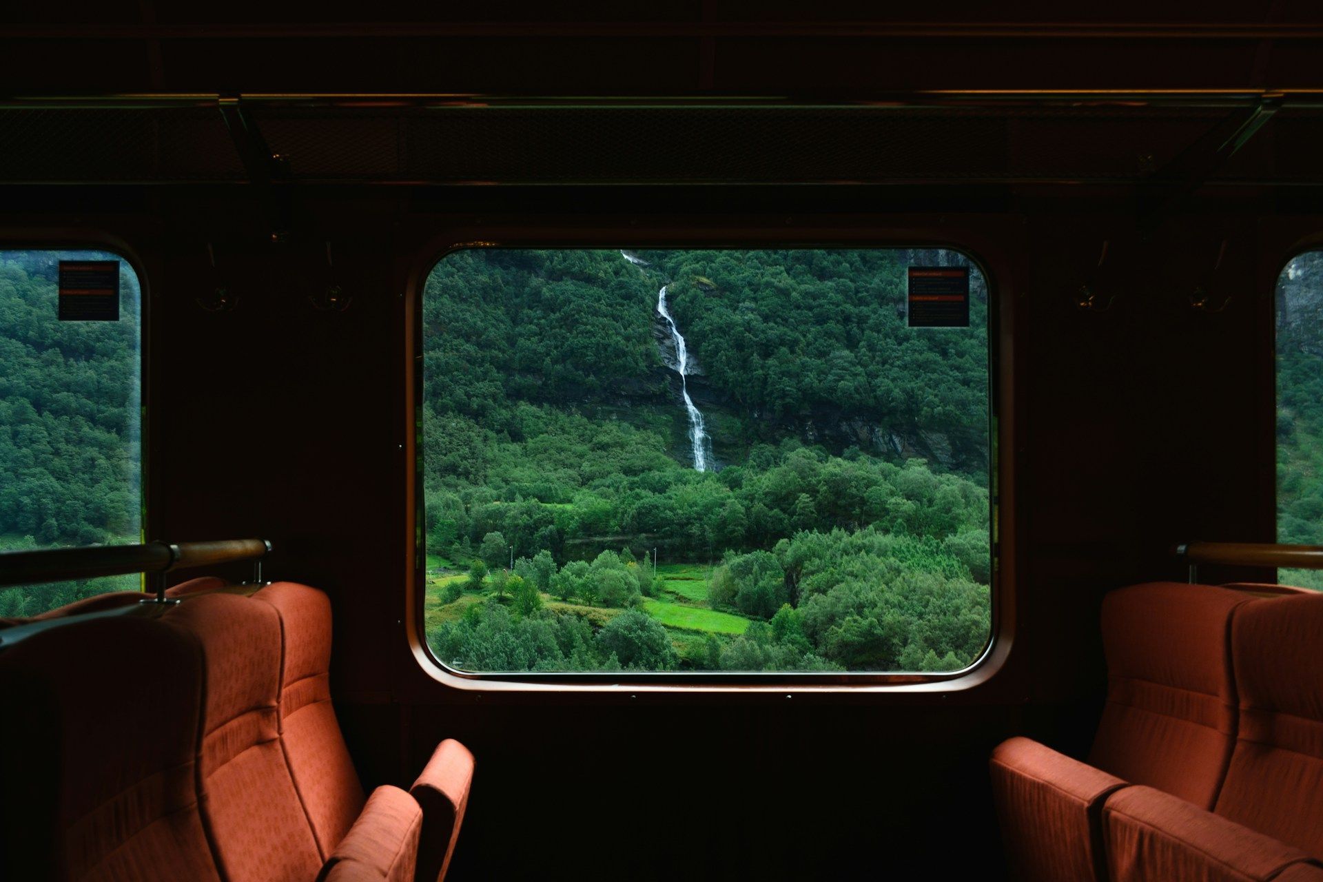 Train traveling across a curved stone bridge in a valley, surrounded by mountains and trees; autumn colors.