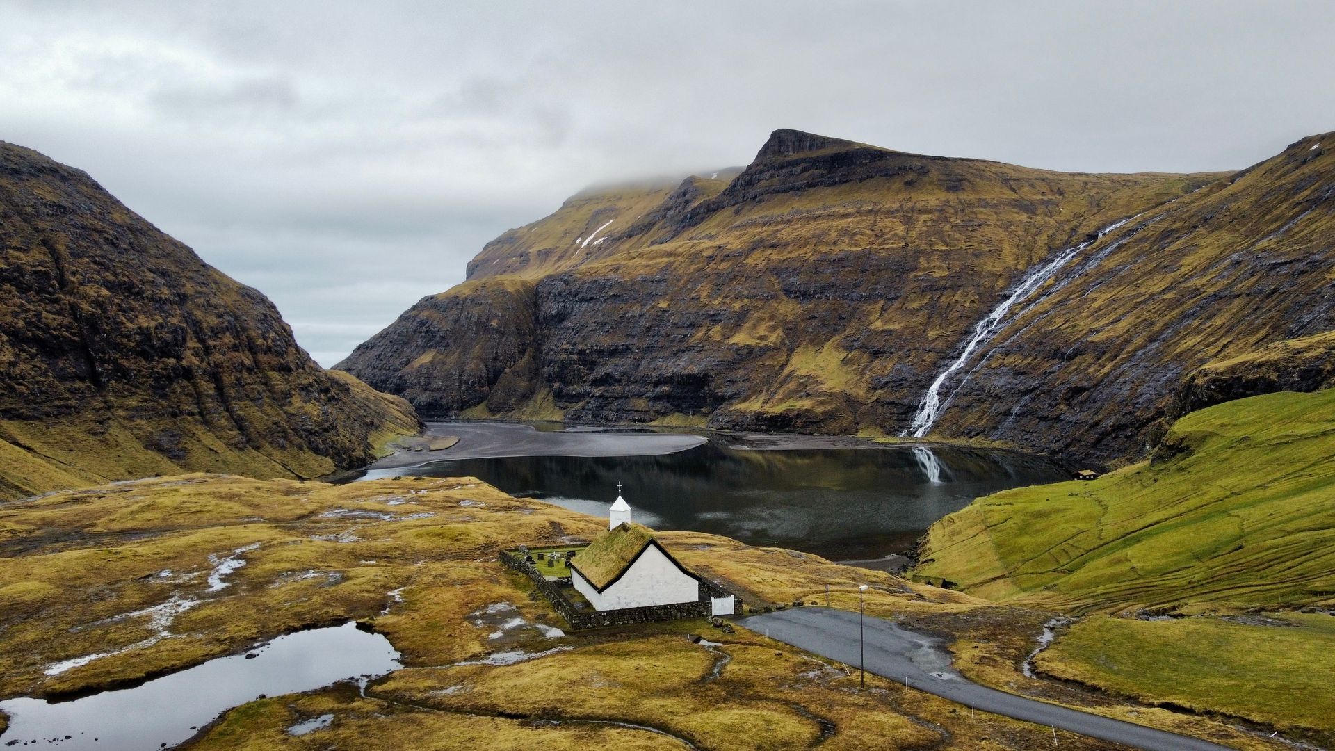 Et lite hvitt hus ligger midt i en dal omgitt av fjell og en innsjø.