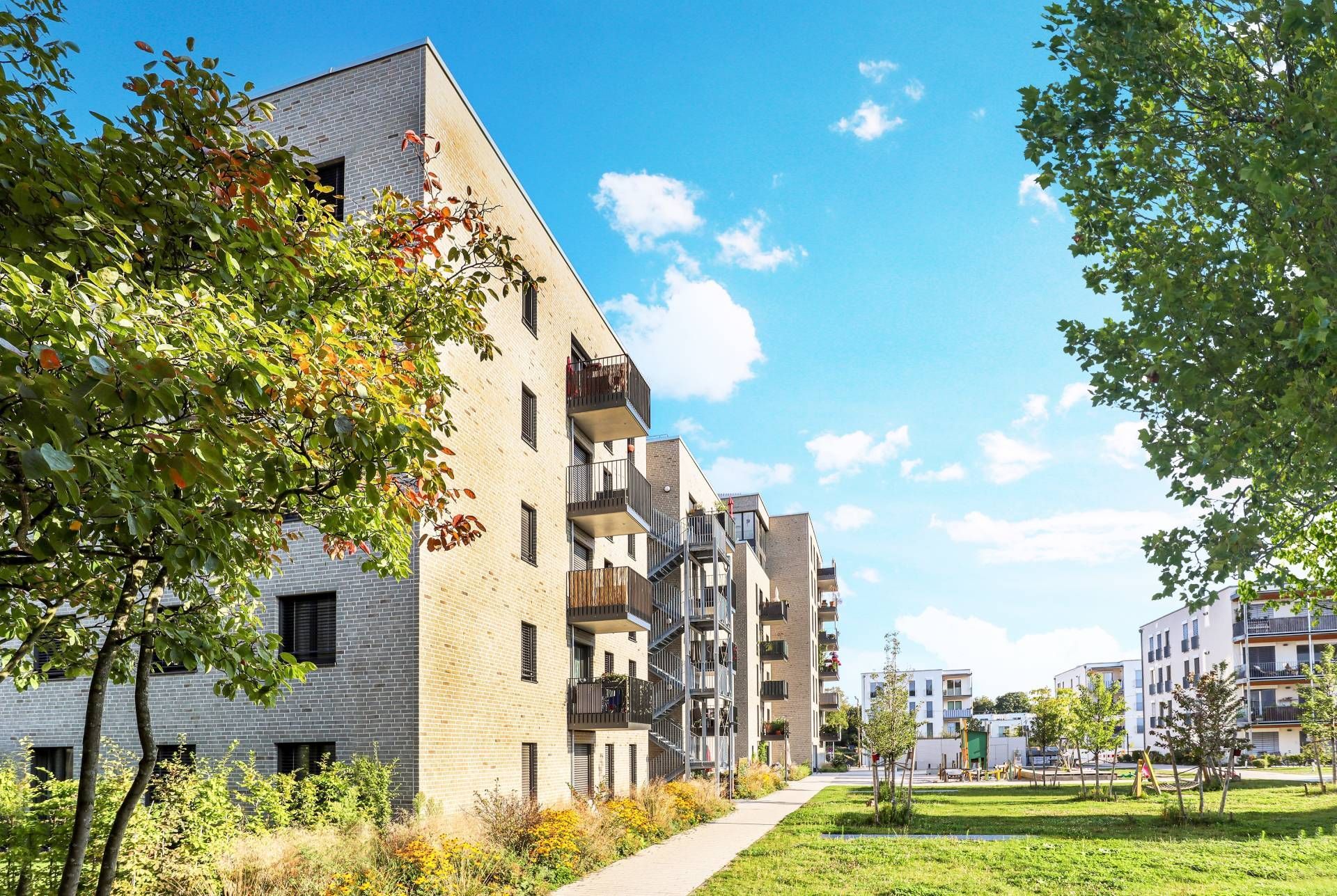Modern apartment buildings beside a green lawn and sidewalk under a bright blue sky