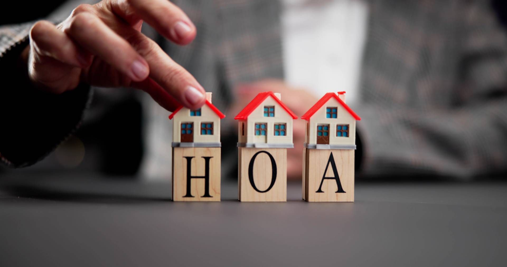 Hand placing a red roof on a wooden HOA block house, with similar houses in the background