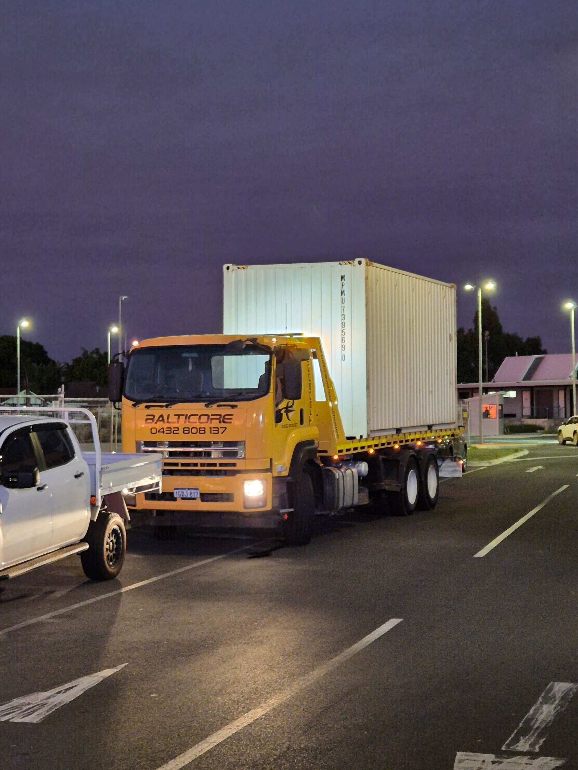 Worker in lift assembling a large metal frame outdoors on a green field under a blue sky.