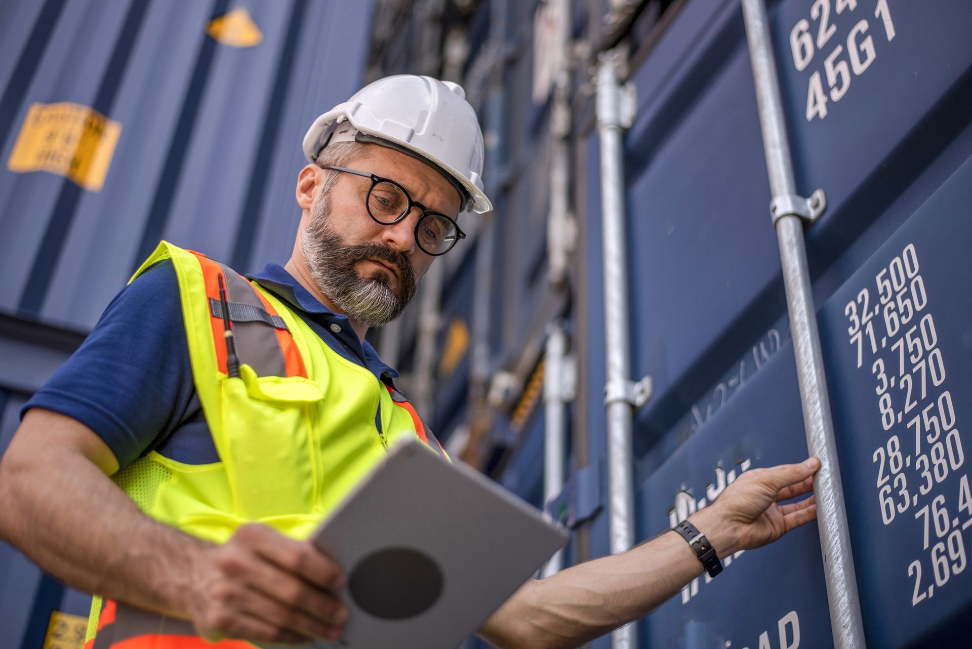 Worker in safety gear inspecting shipping containers.