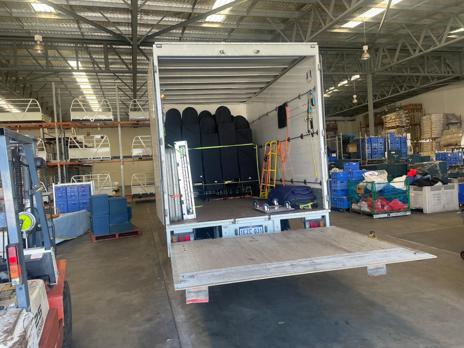 A truck bed loaded with surfboards and equipment, likely for transport, in a warehouse.