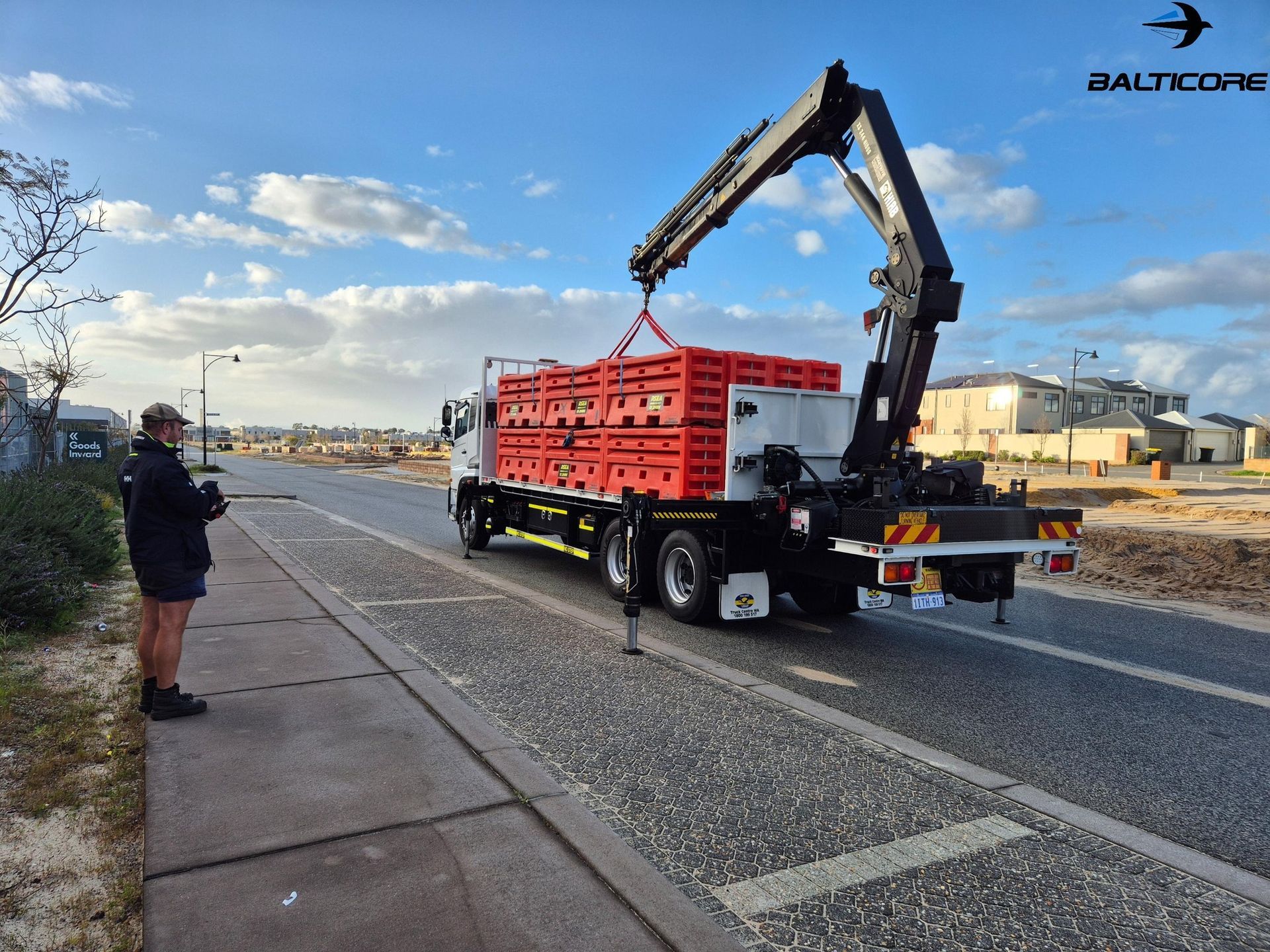 Yellow truck with a white shipping container on a flatbed. It is parked in a lot under the sun.