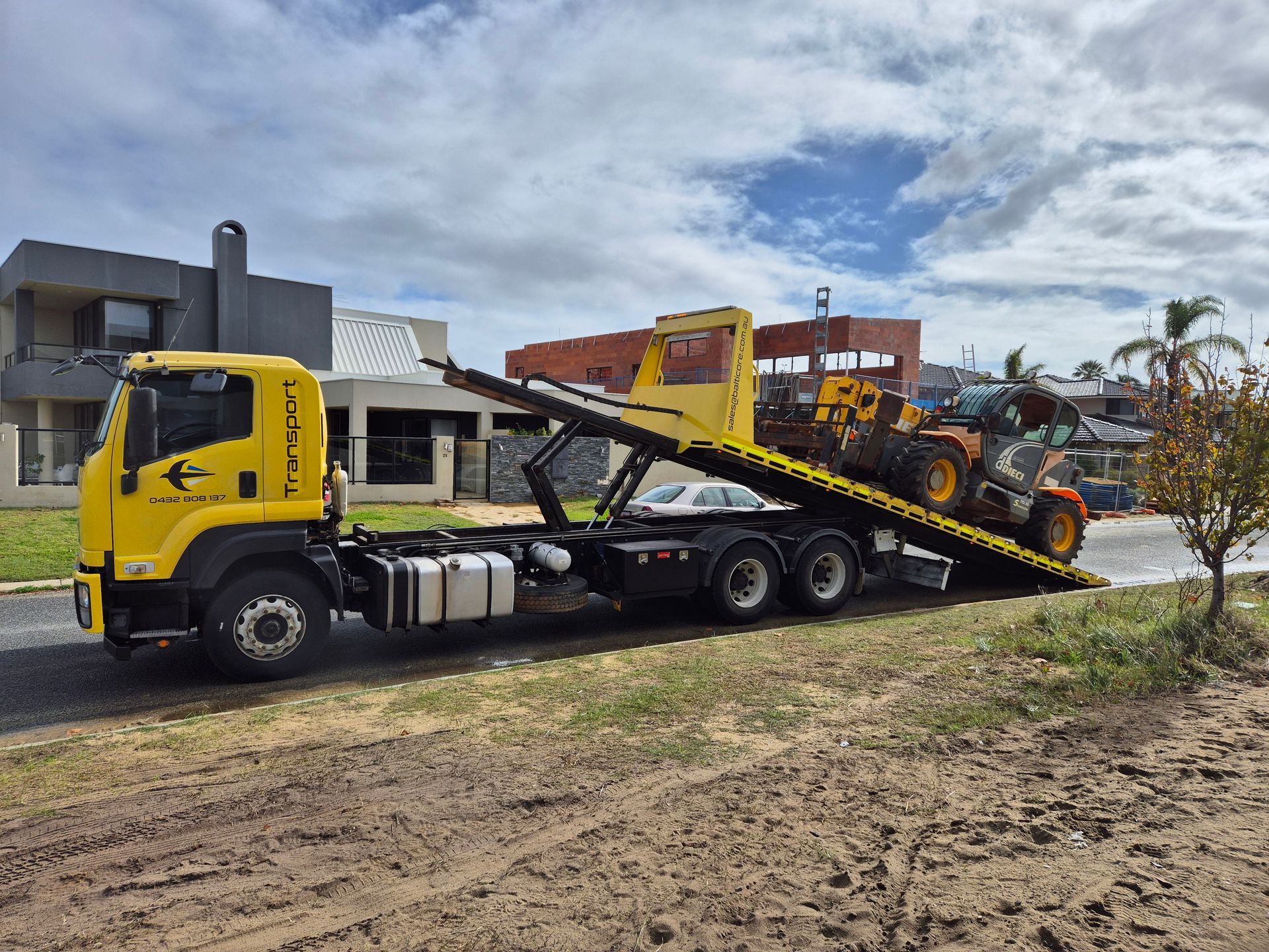 Yellow tow truck carrying construction equipment on a residential street.
