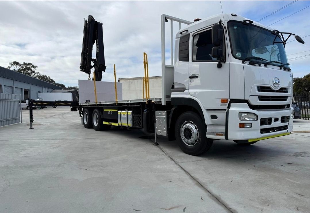 A crane lifting a tan cargo container onto a truck in an outdoor shipping yard.