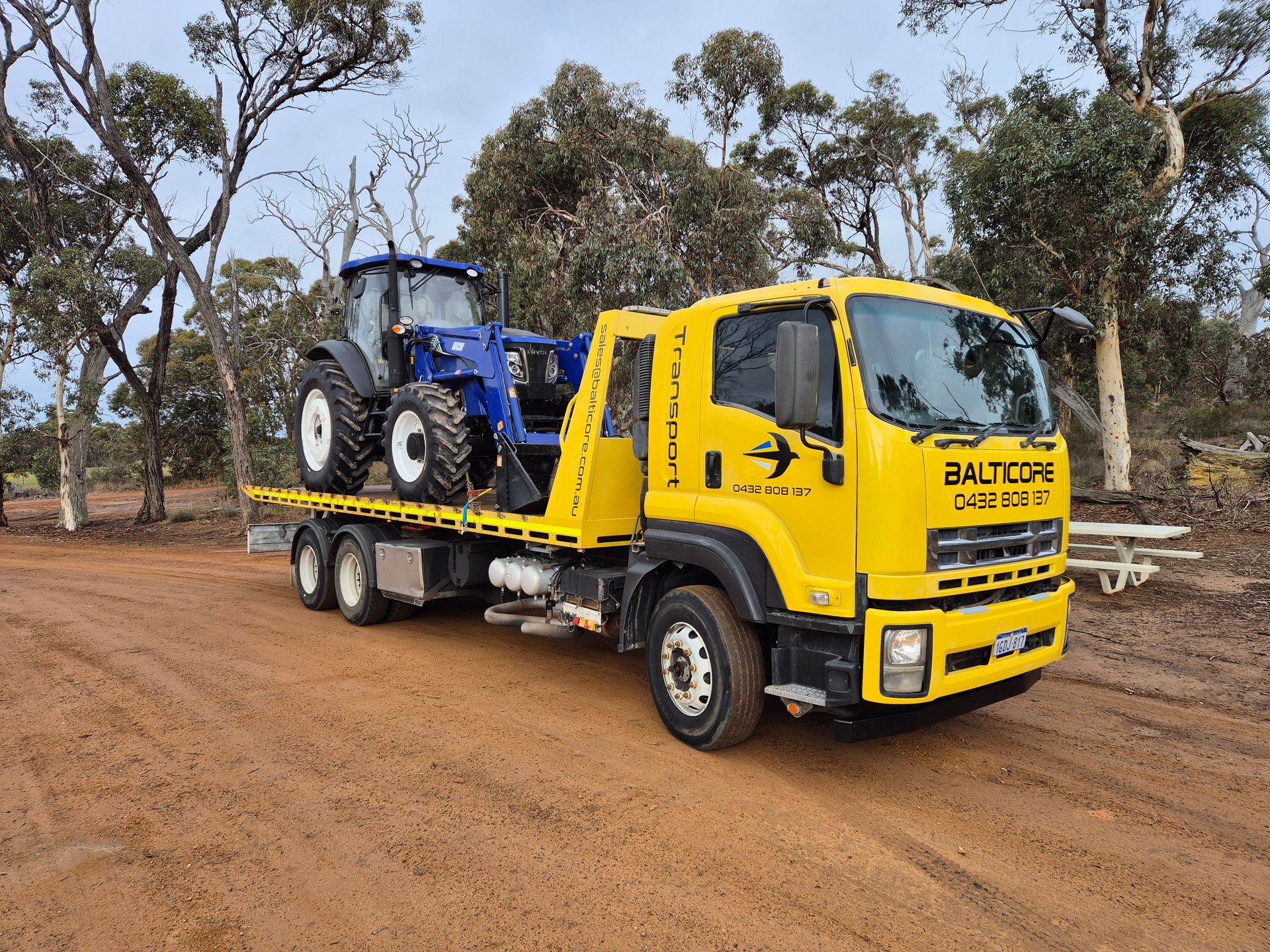 A tractor on a flatbed truck in a grassy field under a cloudy sky.