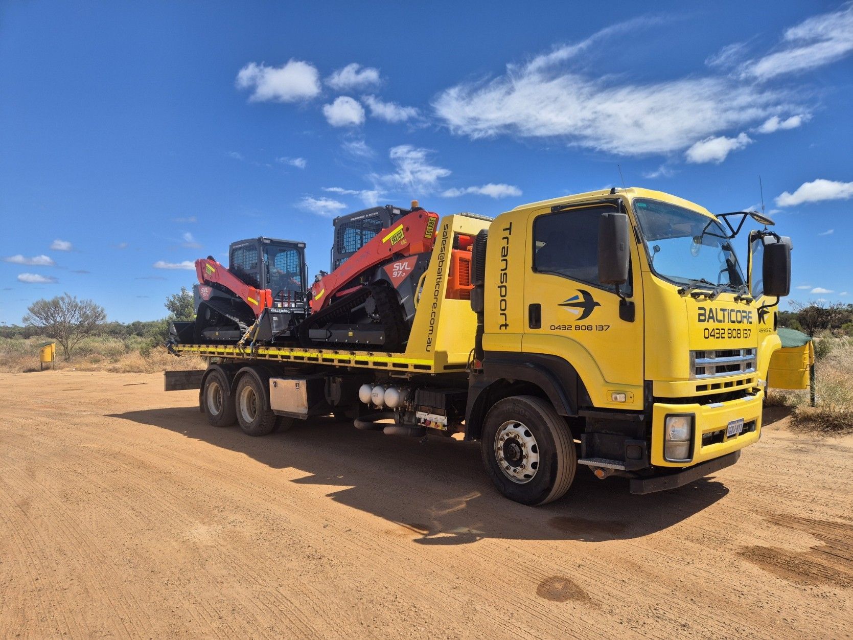 A tractor on a flatbed truck in a grassy field under a cloudy sky.