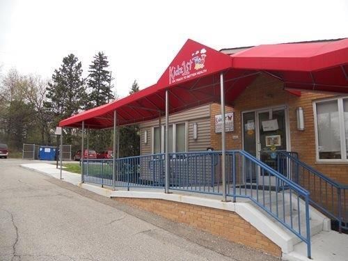 Building entrance with red awning, blue railings, and wheelchair-accessible ramp on a cloudy day