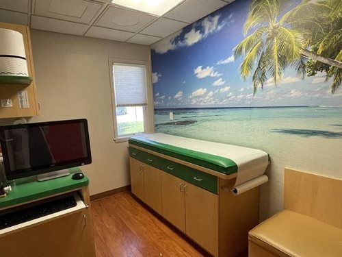 Medical exam room with TV, exam table, and beach mural wall decor