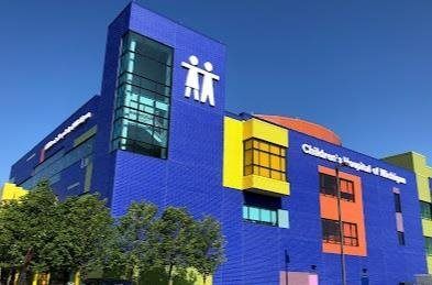 Blue and colorful LEGO-like building with white logo, set against a clear sky and trees