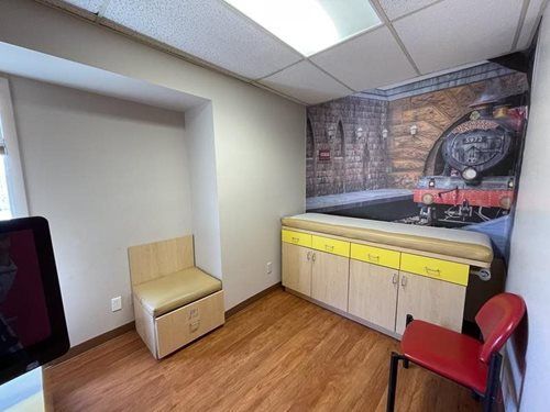 Small break room with cabinets, countertop, red chair, bench, and train mural on the wall.