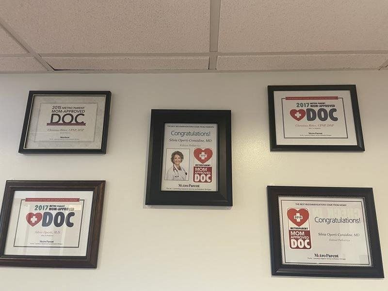 Five framed awards and certificates on a beige wall, including several red heart DOC logos.