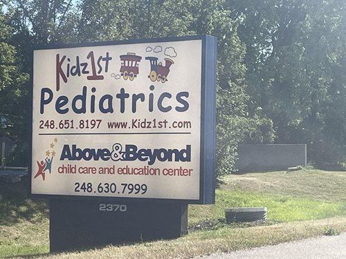 Kid2K Pediatric and Above&Beyond child care sign outdoors by trees