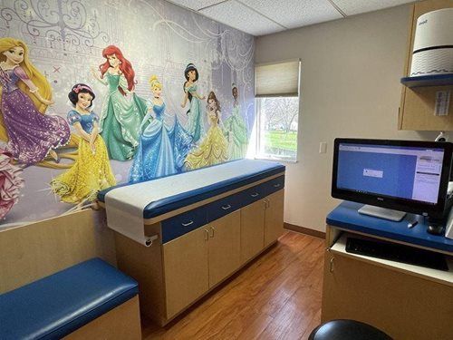 Pediatric exam room with princess mural, exam table, bench, and computer desk