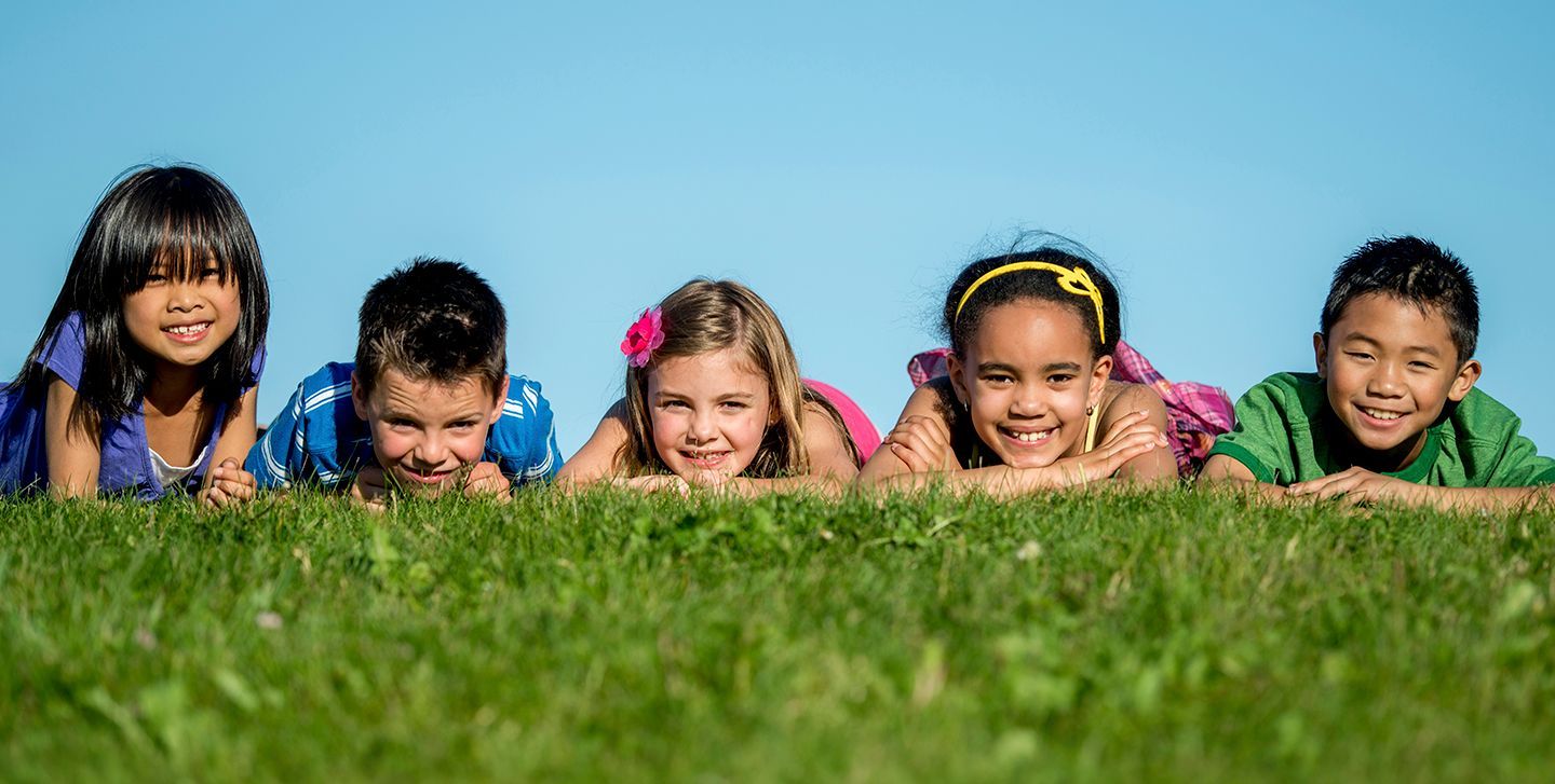 Five children lying in grass, smiling and looking toward the camera.