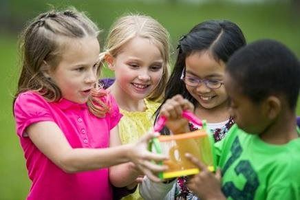 Children in colorful shirts playing together outdoors and passing a small toy cube