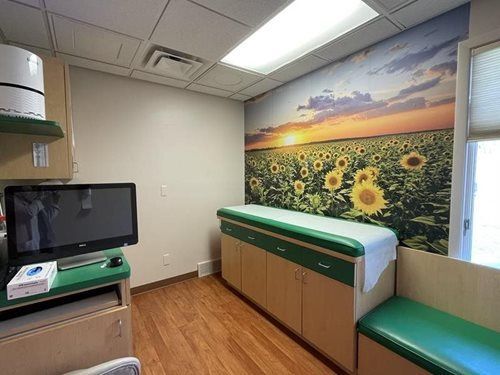 Exam room with a sunflower mural, exam table, bench, and medical monitor on a cabinet