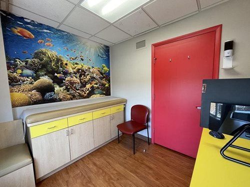 Small office room with coral reef mural, cabinets, red door, chair, and desk computer