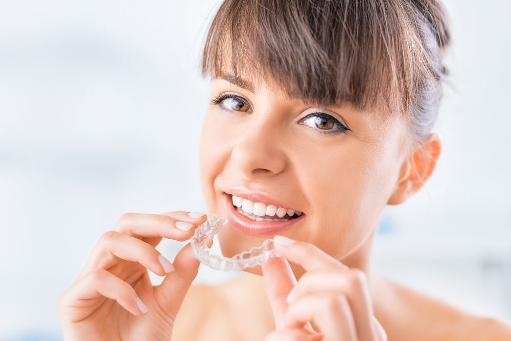 A Person Smiling While Holding a Clear Plastic Dental Aligner — Killara Dental in East Killara, NSW