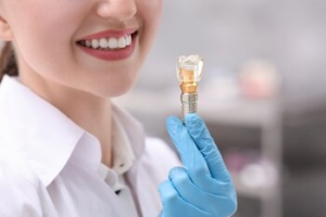 A Professional in a White Coat and Blue Gloves Holds a Dental Implant — Killara Dental in East Killara, NSW