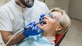 A Dentist in a White Coat and Face Shield Performs a Dental Procedure — Killara Dental in East Killara, NSW