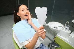 A Person Sitting in a Dental Chair, Wearing a Bib, Holds a Tooth-shaped Mirror — Killara Dental in East Killara, NSW