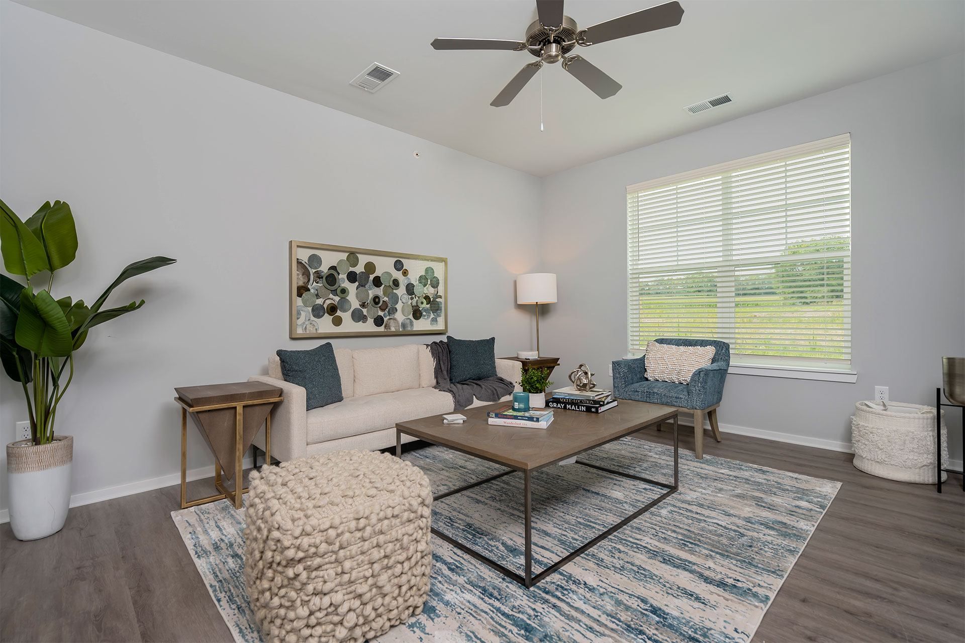 A living room with a white ceiling fan and a large window with blinds.