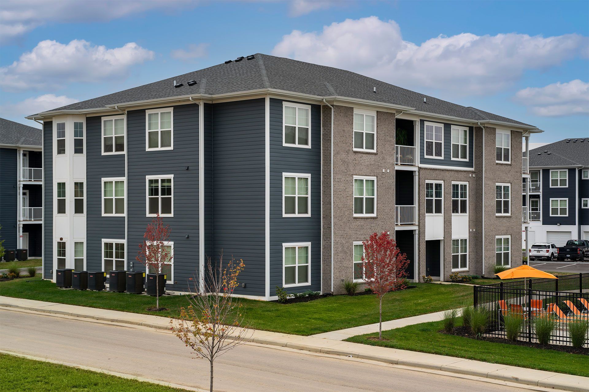 Apartment building with grey and white exterior and a small tree in front.