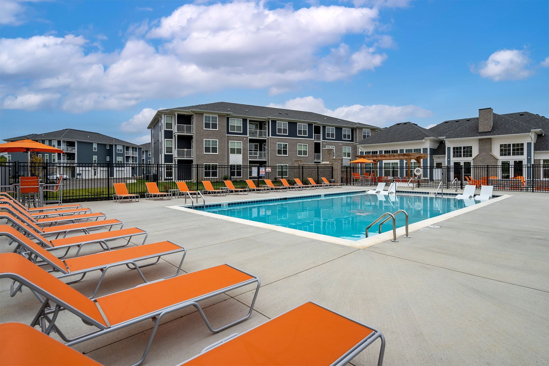 A swimming pool surrounded by orange sun loungers and a building in the background.