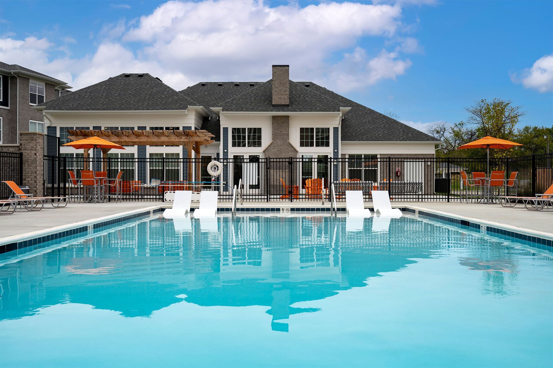 A swimming pool in front of a house with orange chairs around it.