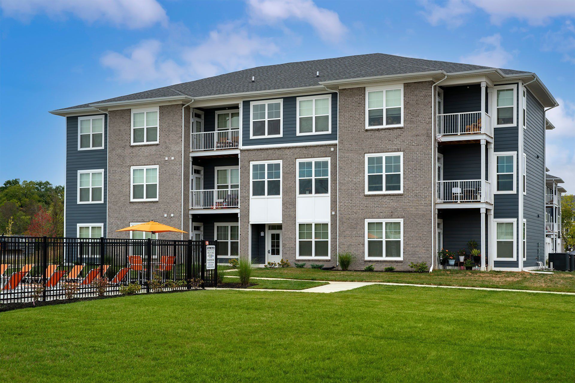 A large grey apartment building with a black fence in front.