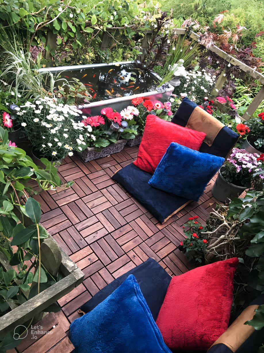 A wooden deck with red , blue and black pillows and a pond in the background.