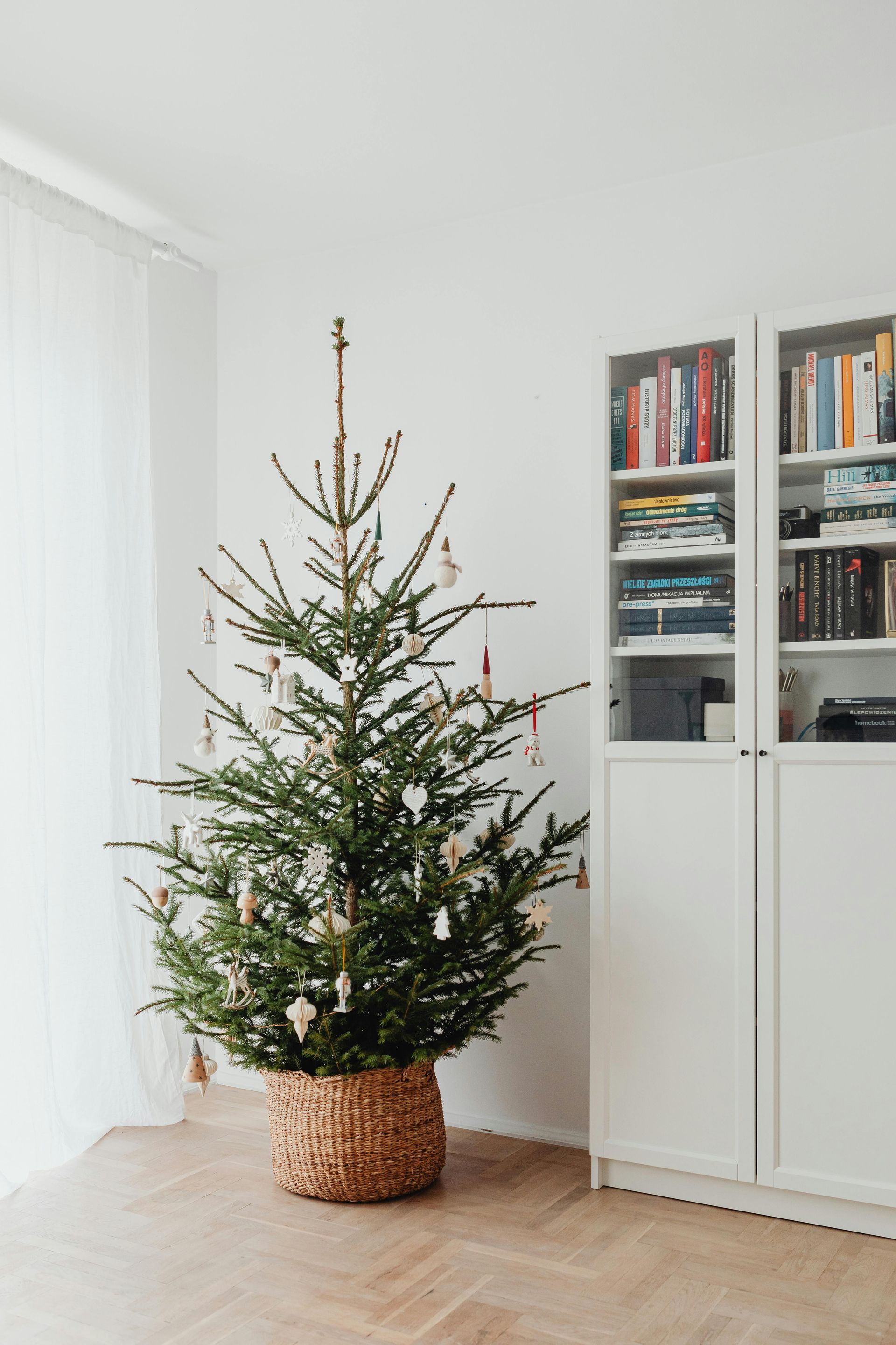 A white wallpapered living room with Christmas tree and bookcase.