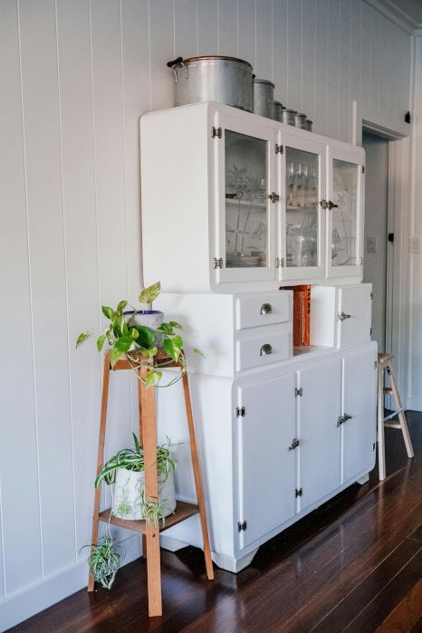 A white cabinet with glass doors and drawers is in a room next to a wooden ladder.