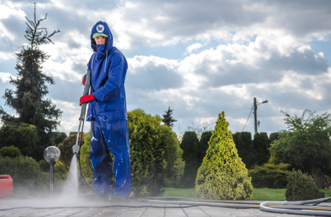 Person in blue protective suit using a power washer on a wooden deck, creating mist.